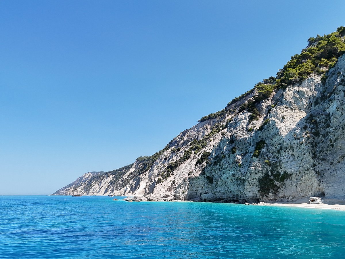 A luxury yacht anchored in a turquoise bay next to a whitewashed village.